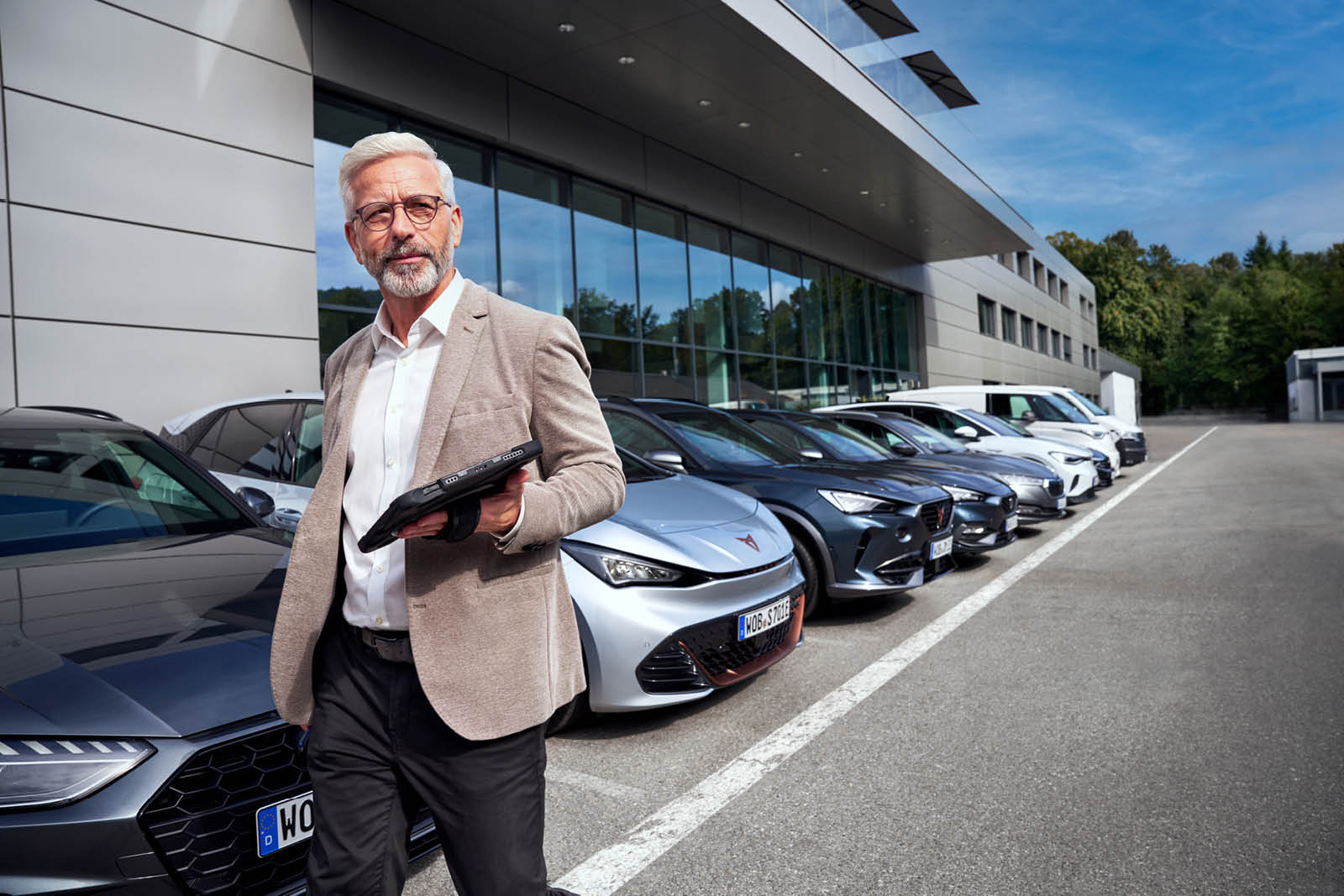 Mitarbeiter mit Tablet in der Hand stehr vor Fahrzeugflotte