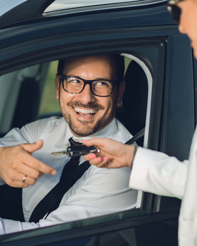 Mann sitzt im Auto und erhält einen Autoschlüssel von einer Dame überreicht